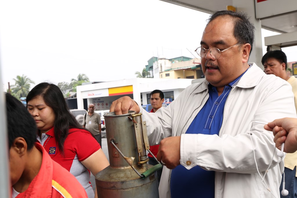 DOE Usec. Donato D. Marcos inspects a calibrating bucket to check compliance with standards for liquid petroleum products sold by gasoline stations/retail outlets.